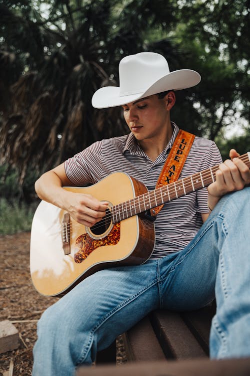 Free Man in Hat Sitting and Playing Guitar Stock Photo