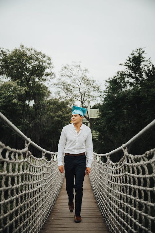 Free A man in a blue shirt and white hat is walking on a rope bridge Stock Photo