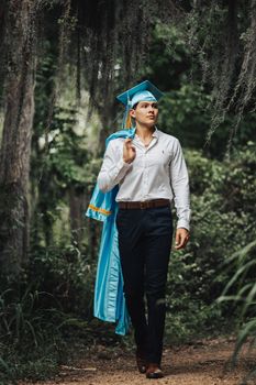 Young adult in graduation attire, walking confidently in a serene forest setting. Success and accomplishment themes.