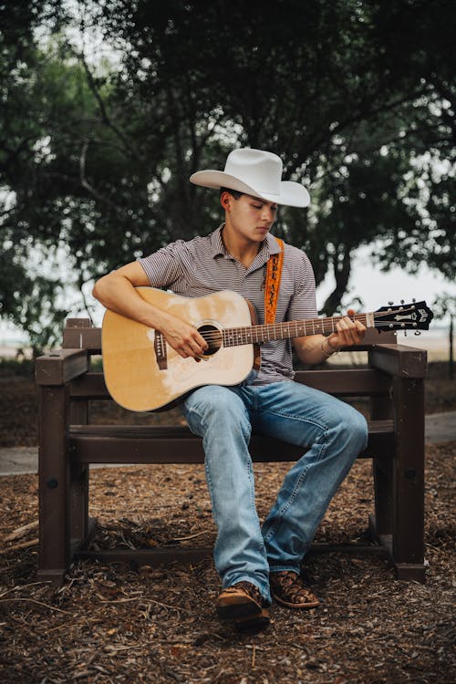 Free A man in cowboy hat sitting on a bench playing guitar Stock Photo