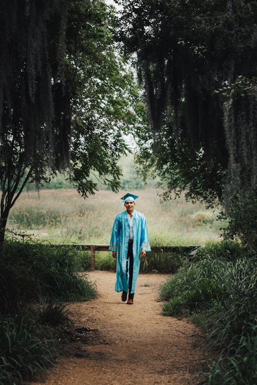 Free A man in a blue graduation gown walks through a forest Stock Photo