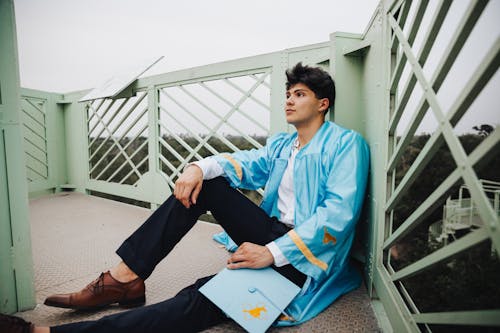 A young man in a blue robe sitting on a bridge