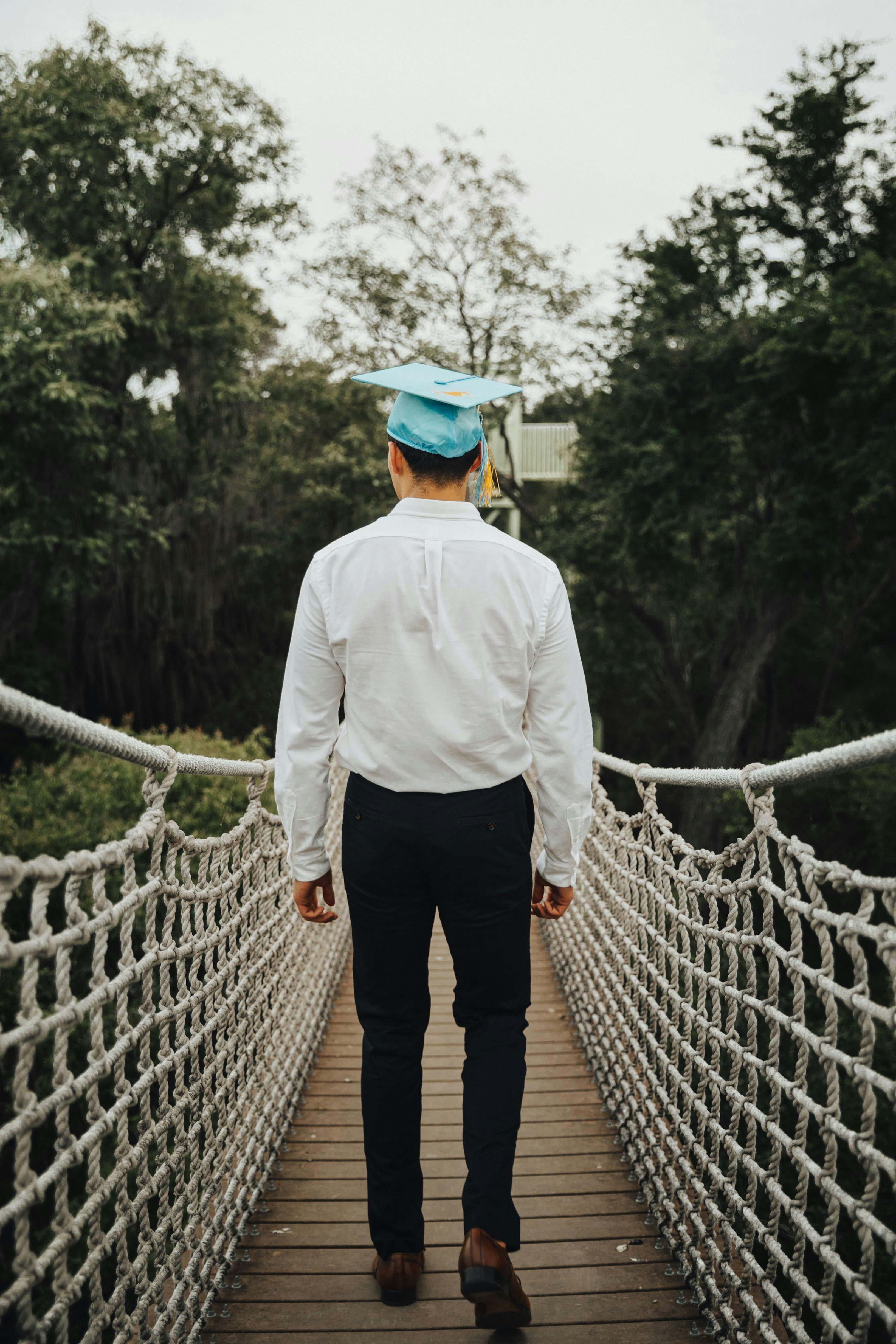 man in shirt and academic hat walking on footbridge