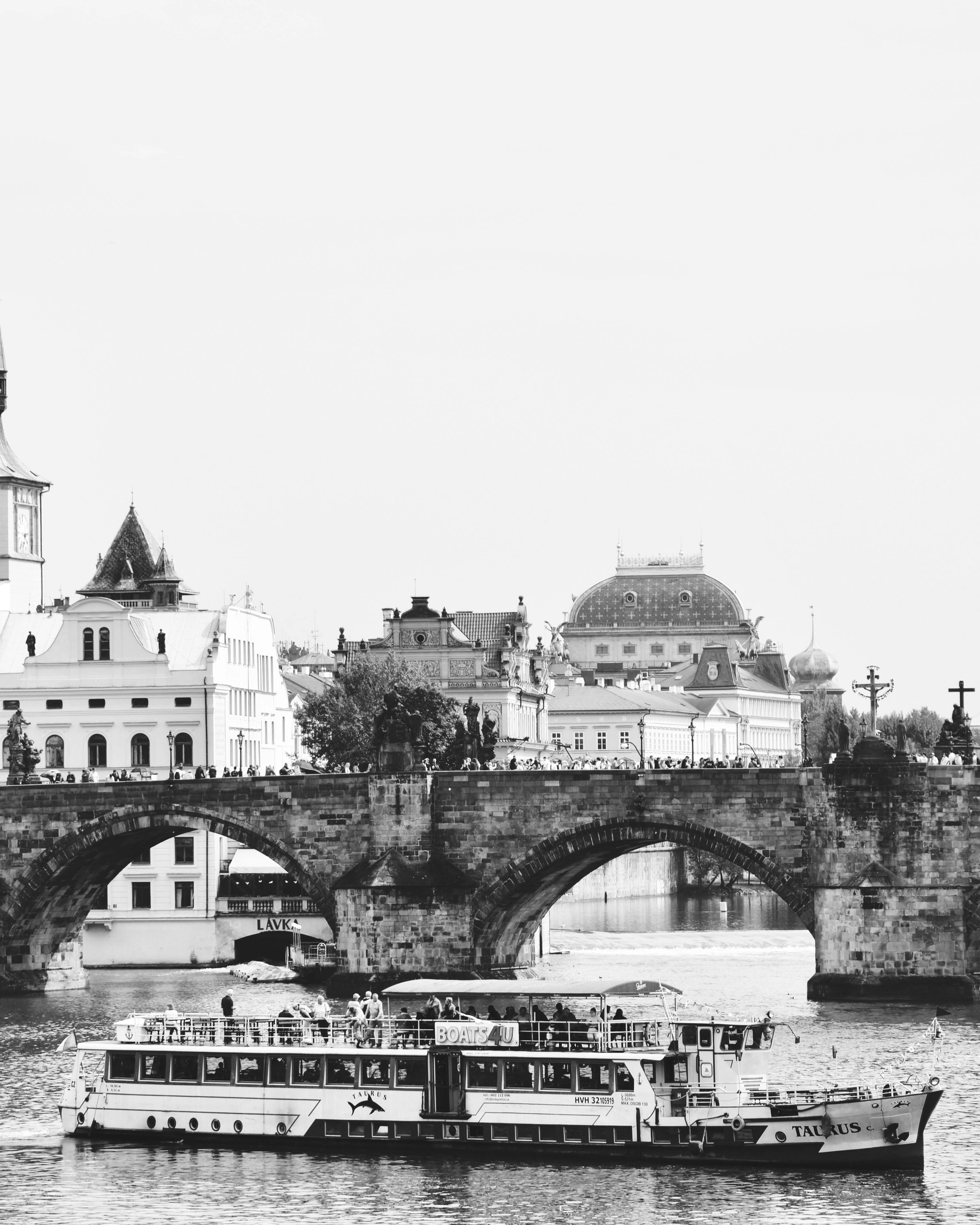 Black and white photo of the Charles Bridge in Prague with a passenger boat on the Vltava river.
