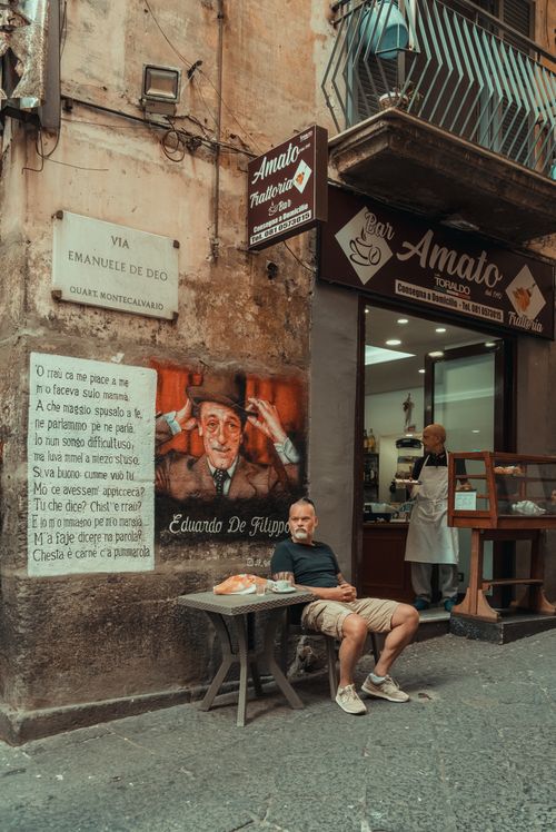 Free Man relaxing at a cafe in the streets of Napoli, Italy with street art and bakery backdrop. Stock Photo