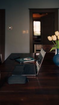 Cozy home office setting featuring laptop on wooden table with vase of tulips.