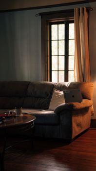 A cozy living room setup featuring a sofa, laptop, and warm lighting by a window.