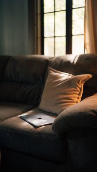Sunny corner of a cozy living room with a laptop on the sofa and natural window light.