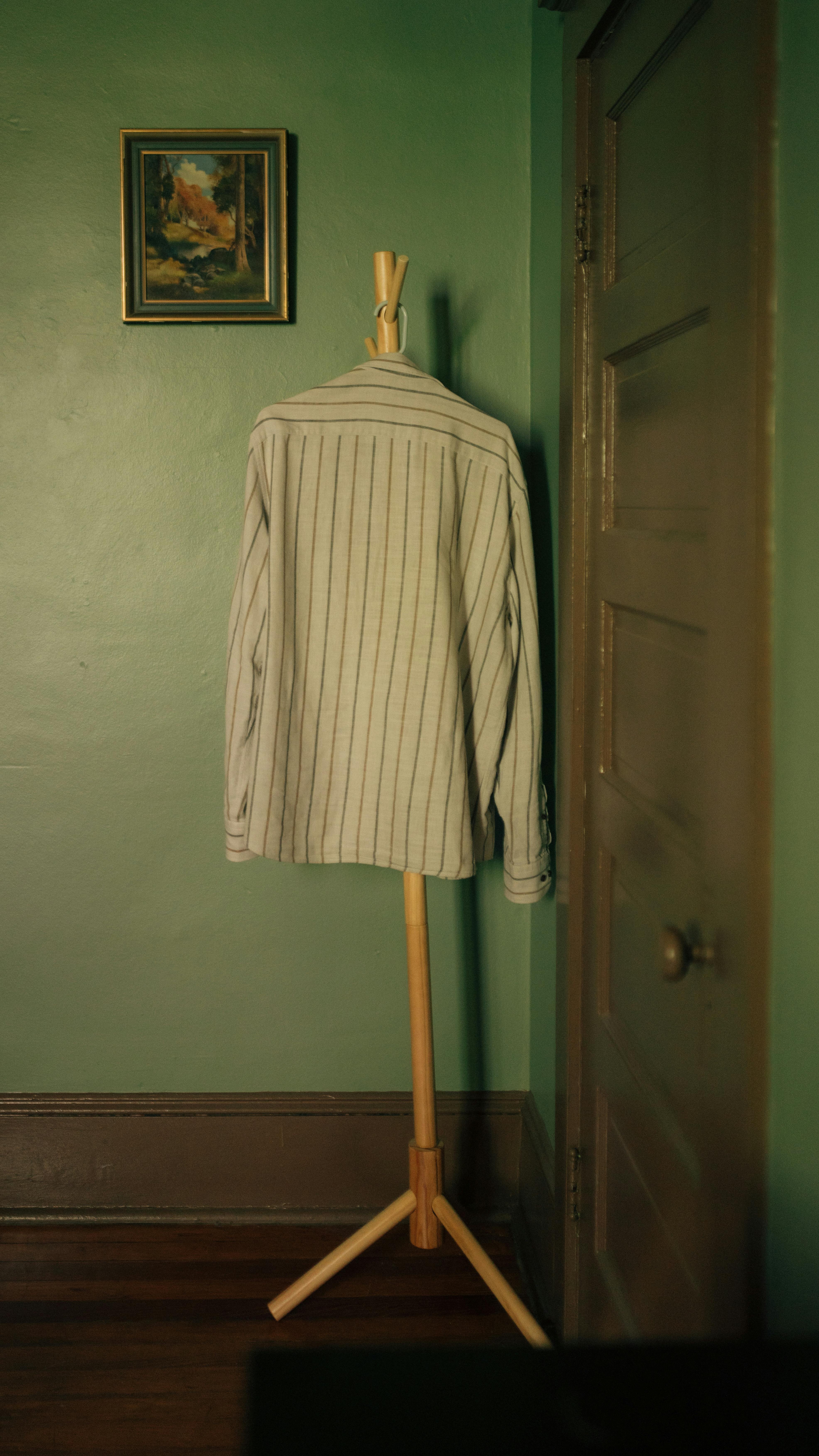 Free A striped shirt draped on a wooden stand against green walls, with a vintage painting nearby. Stock Photo
