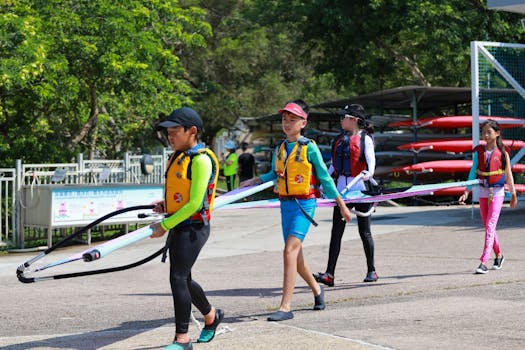 Group of children carrying windsurf boards on a sunny outdoor day, enjoying recreational activities.