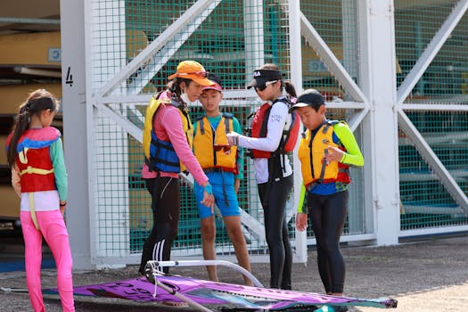 Group of kids and instructor getting ready for a windsurfing lesson outside with equipment.