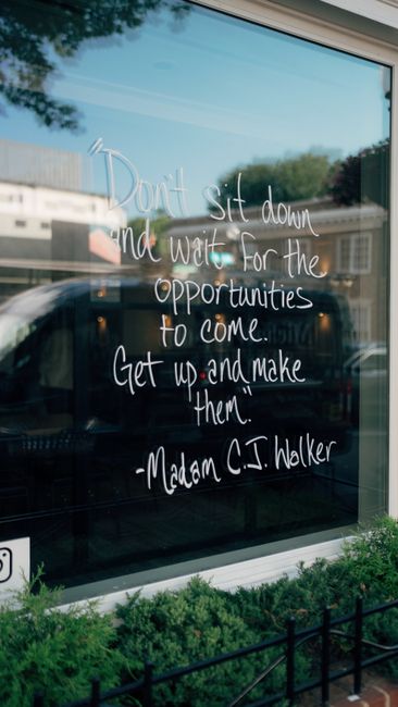 A motivational quote by Madam C.J. Walker written on a glass window reflecting street scenery.