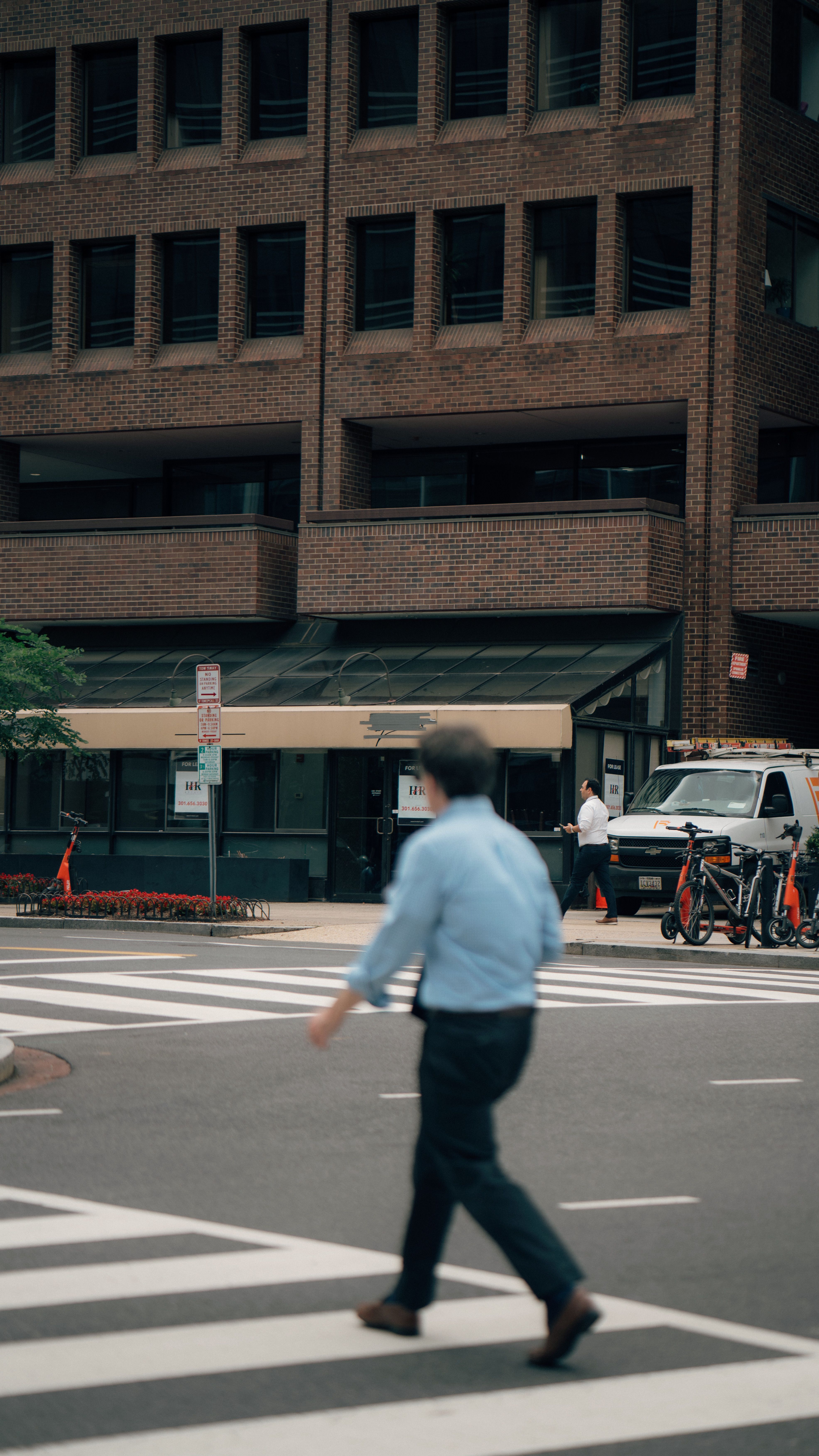 A man walking across a crosswalk in front of a building · Free Stock Photo