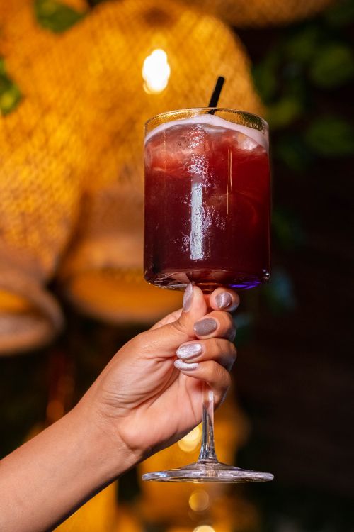 Free Close-up of a woman's hand with manicure holding a cocktail glass in a dimly lit setting. Stock Photo