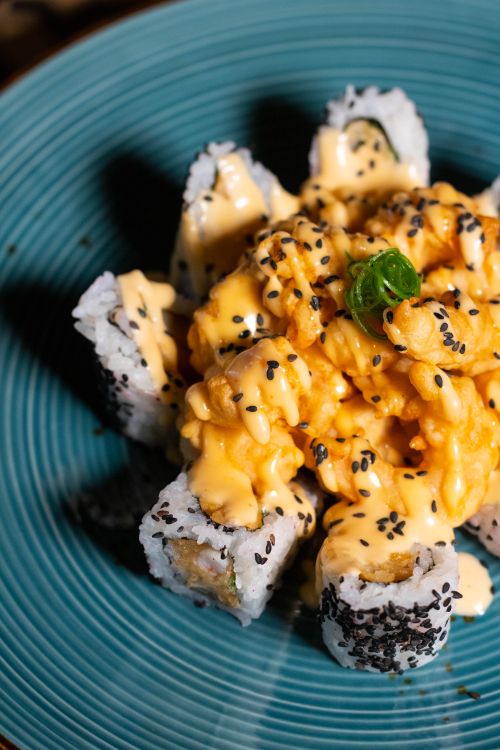 Free Close-up of sushi rolls topped with spicy mayo and black sesame seeds on a vibrant blue plate. Stock Photo