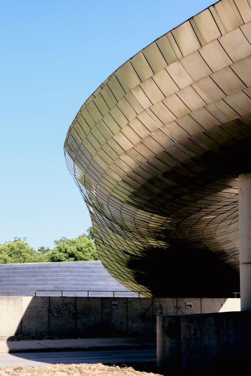 Free Curved architectural structure with metal panels under a clear blue sky. Stock Photo