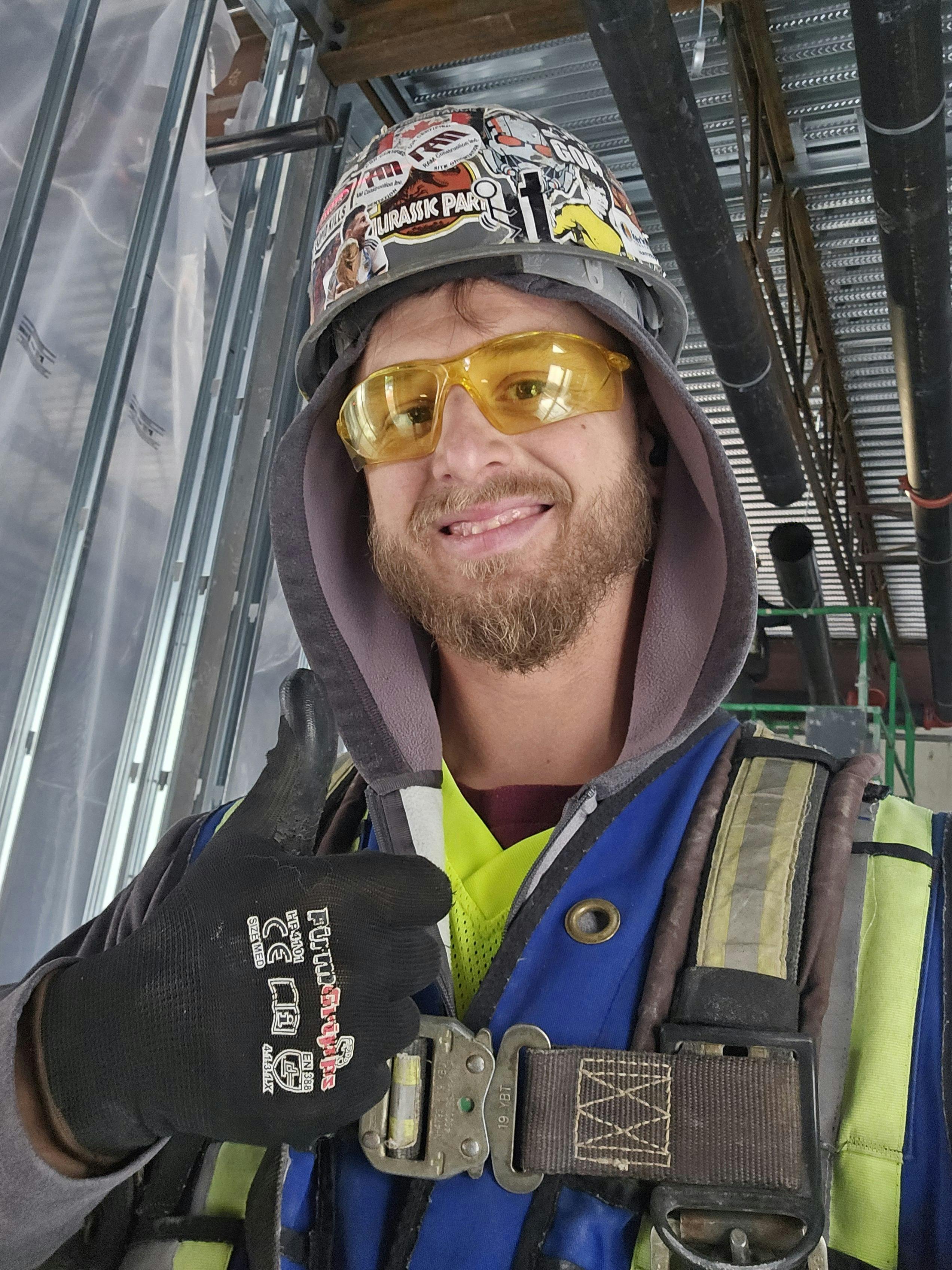 Smiling construction worker wearing safety gear gives a thumbs up at the site.