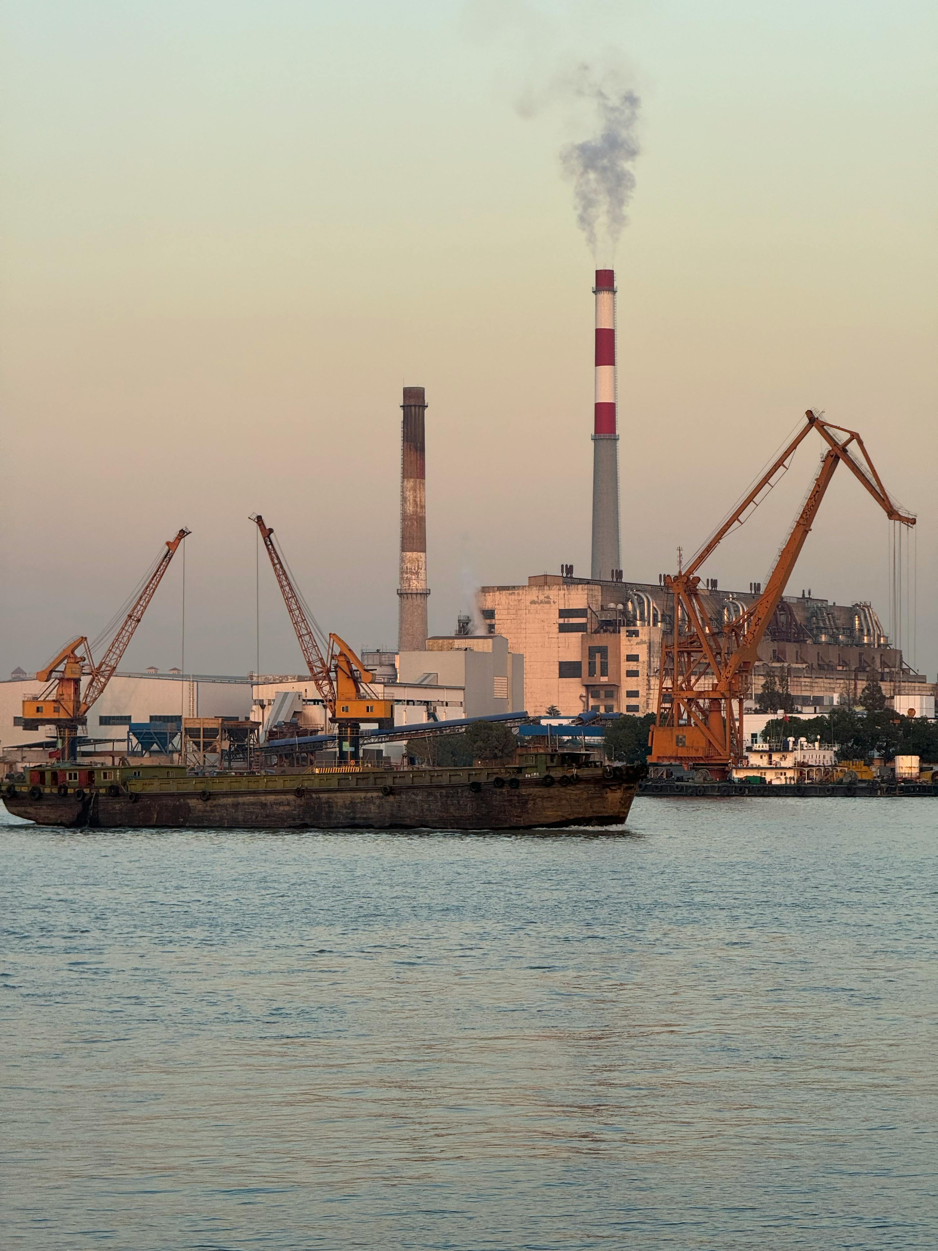 Gün doğumunda nehir kenarında fabrika ve gemi silüeti