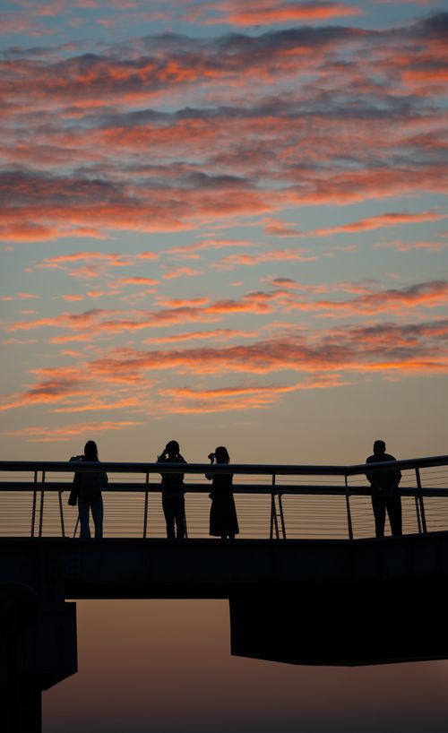 Free Silhouetted people standing on a footbridge against a colorful sunset sky. Stock Photo