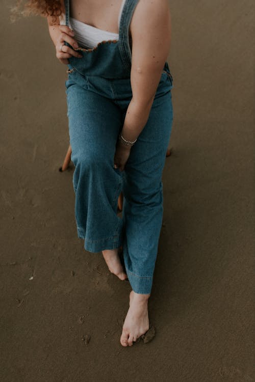 A woman sitting on a beach wearing overalls