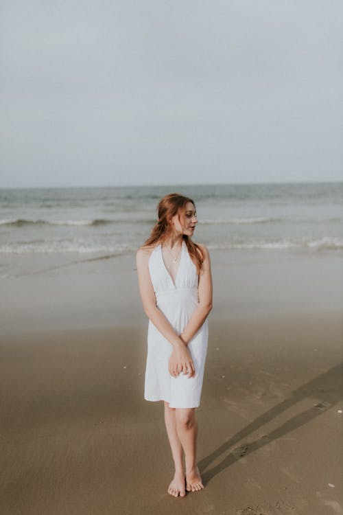 Free A woman in a white dress standing on the beach Stock Photo