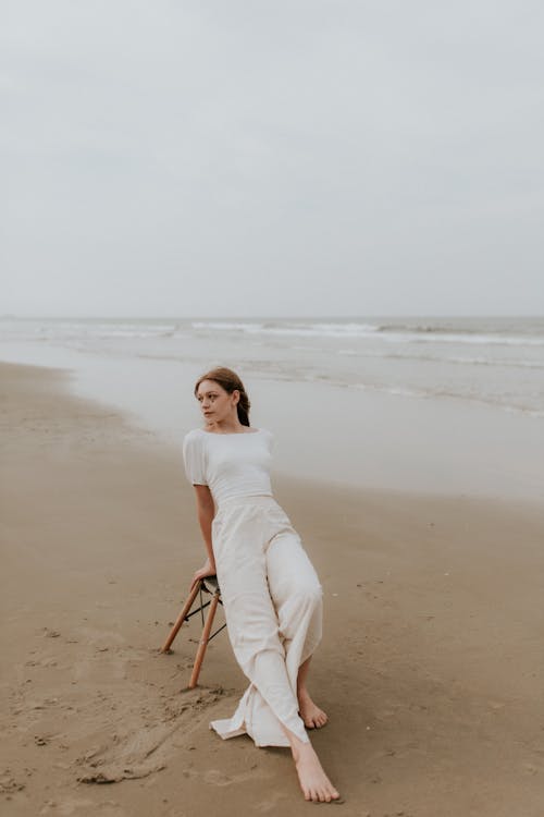 A woman sitting on the beach in a white dress