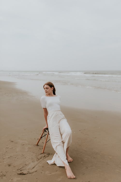 Free A woman sitting on the beach in a white dress Stock Photo