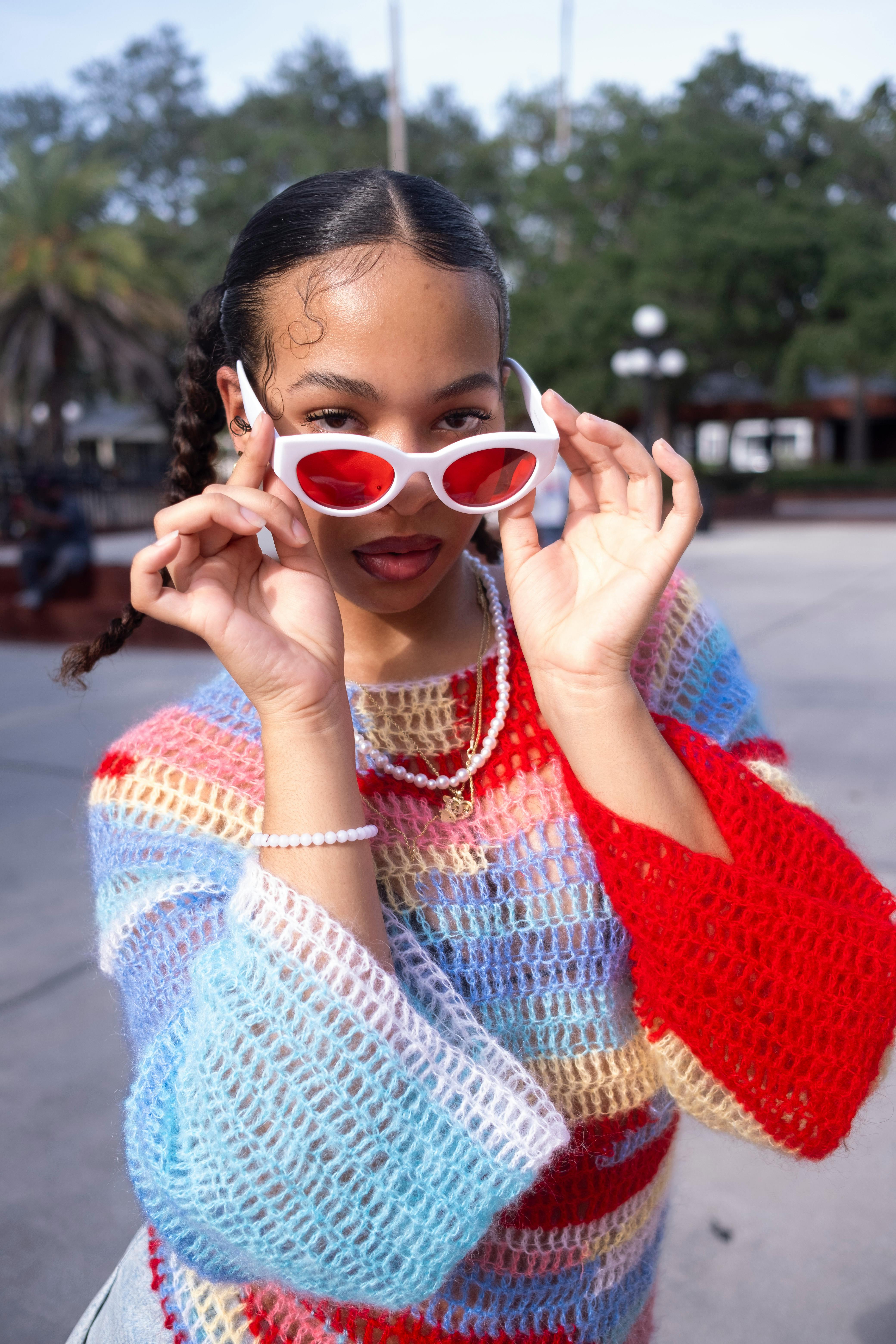 Stylish portrait of a woman wearing colorful knit and red sunglasses outdoors.