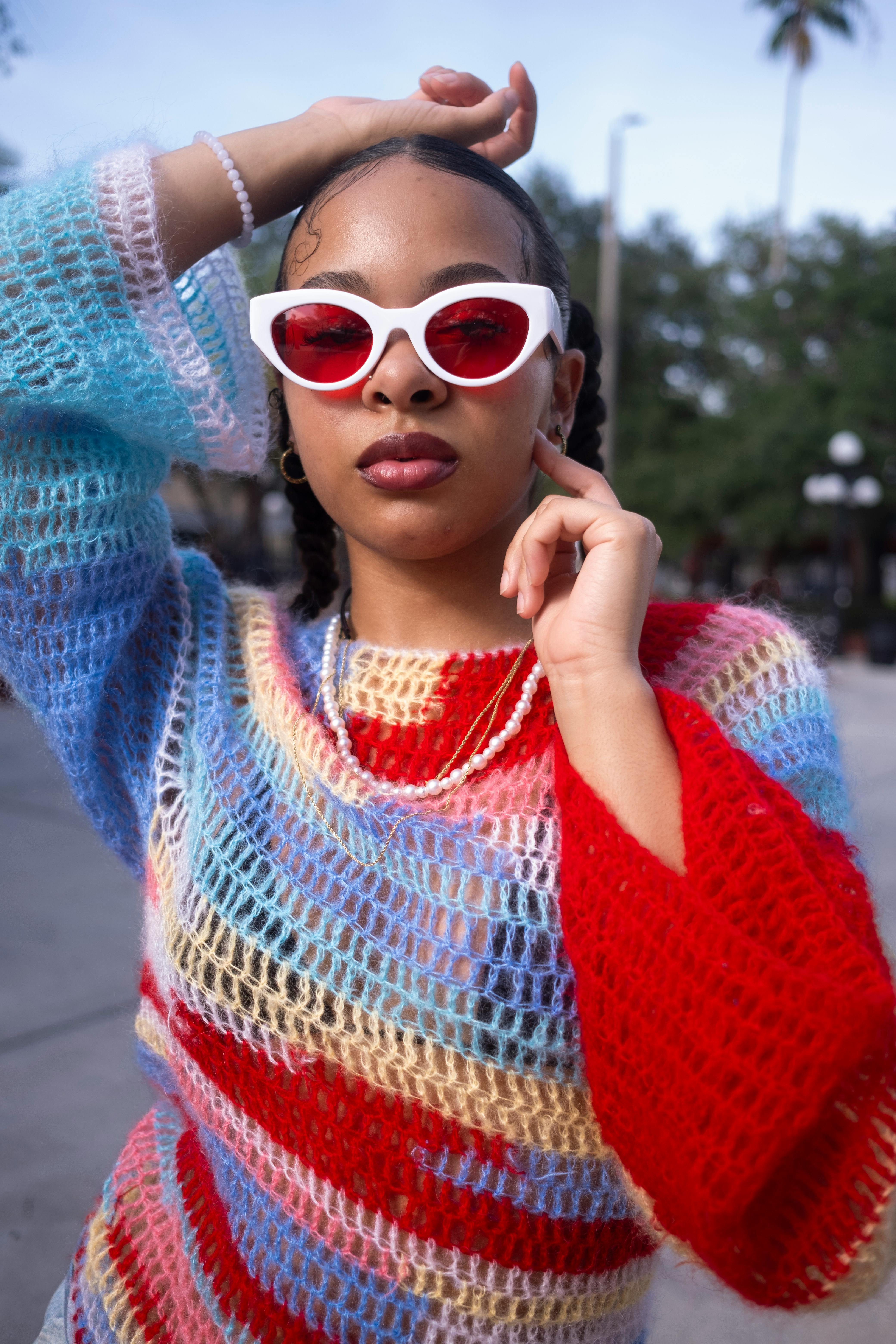 Chic outdoor portrait of a woman in colorful knitwear and red sunglasses.