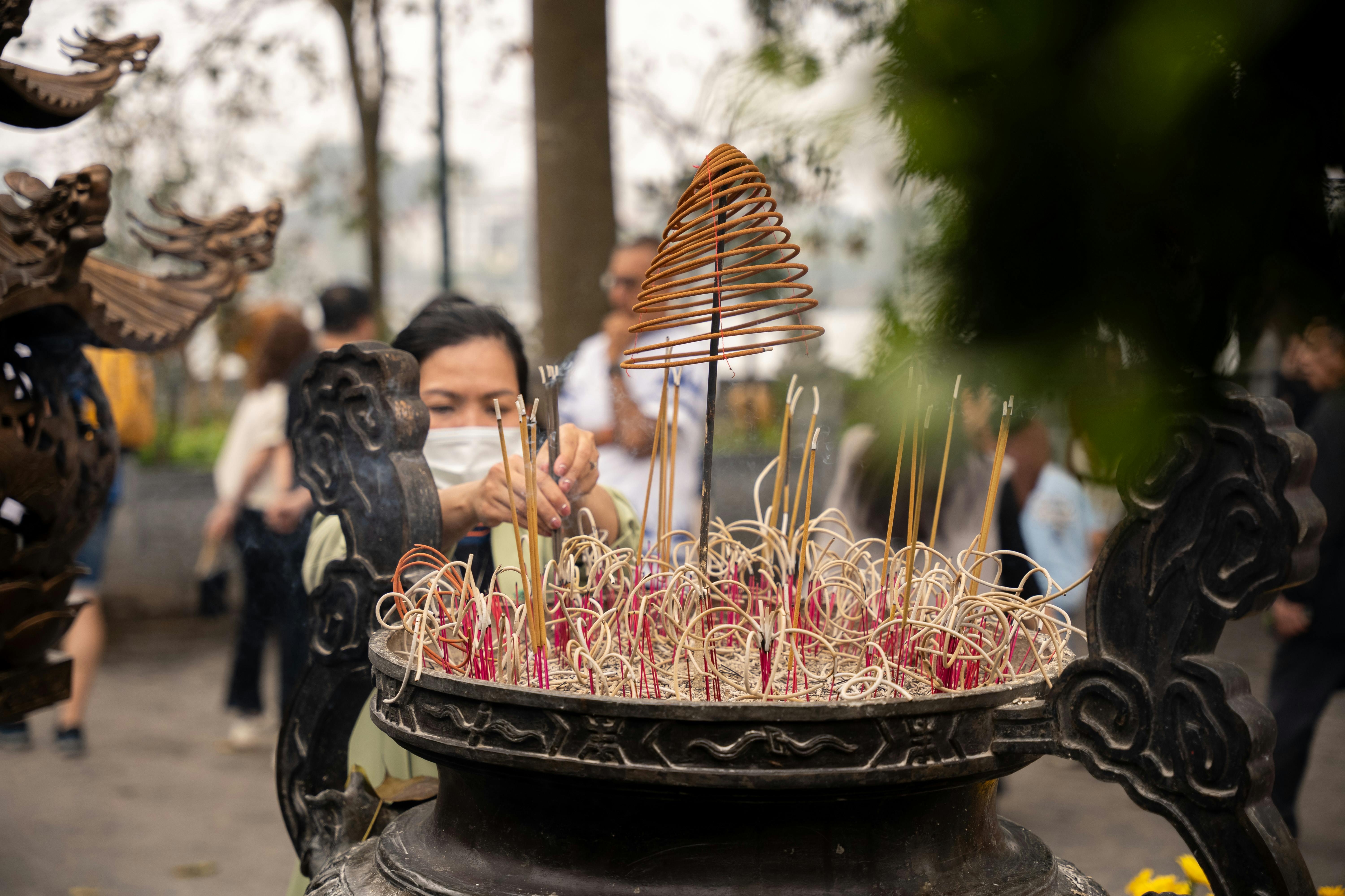 An Asian man lights incense sticks at an outdoor temple, creating a serene religious scene.