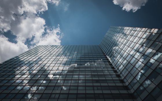 Low angle view of a glass skyscraper in Hamburg reflecting clouds in a clear sky.