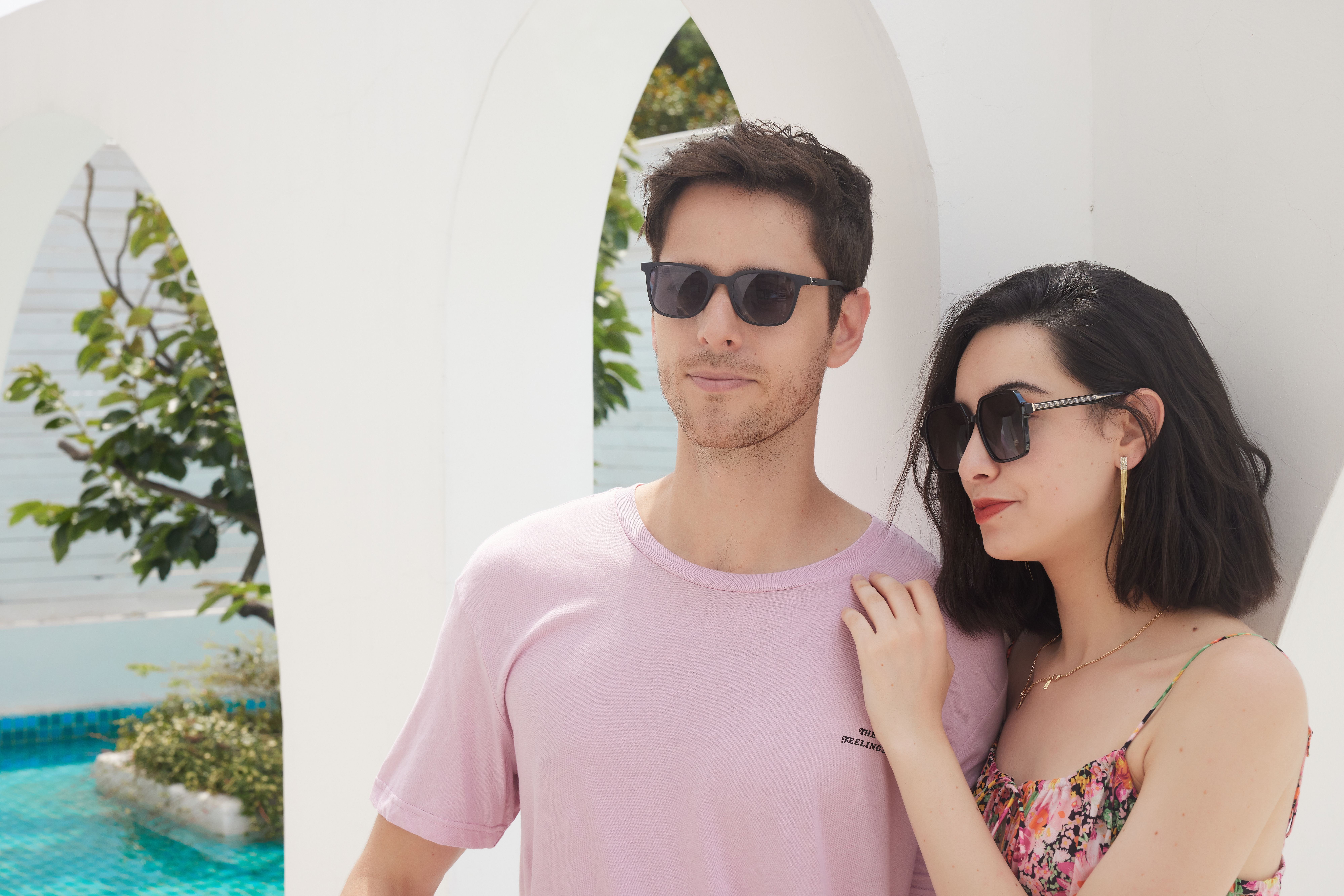 Young couple enjoying sunny weather by a pool, showcasing summer fashion and relaxation.