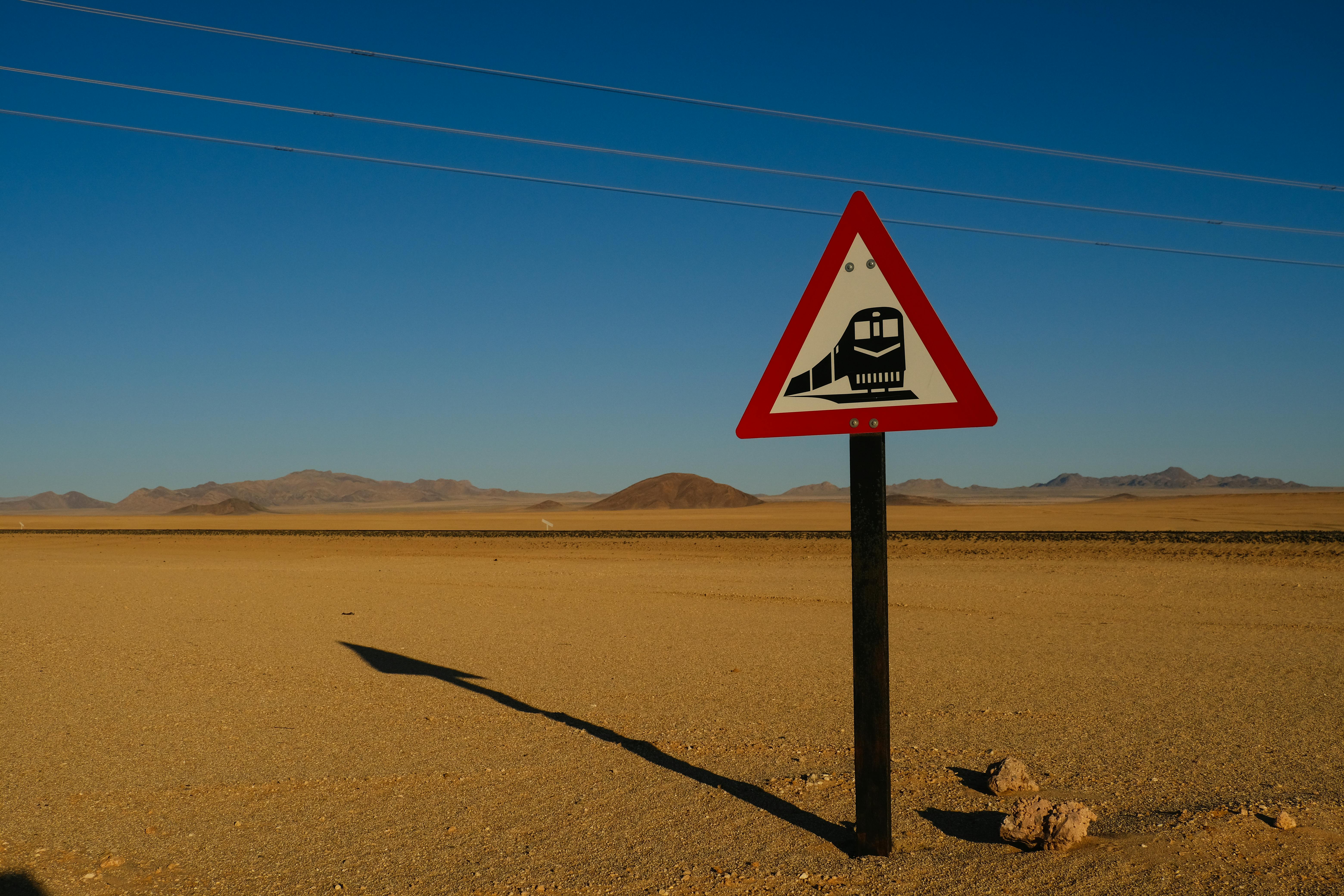 A triangular train crossing sign in a desert with a blue sky backdrop.