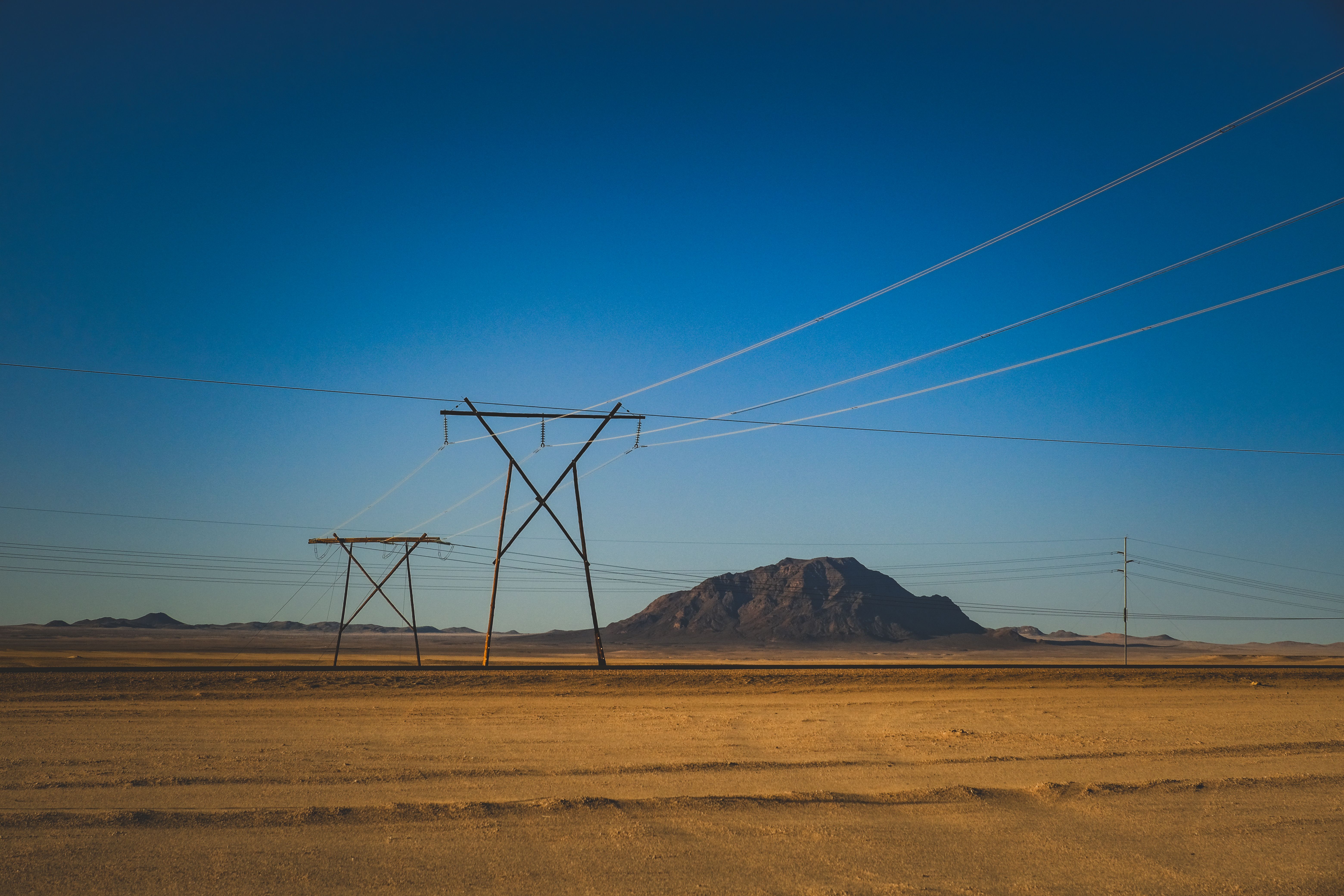 High-voltage power lines crossing a dry desert with distant mountains under a blue sky.