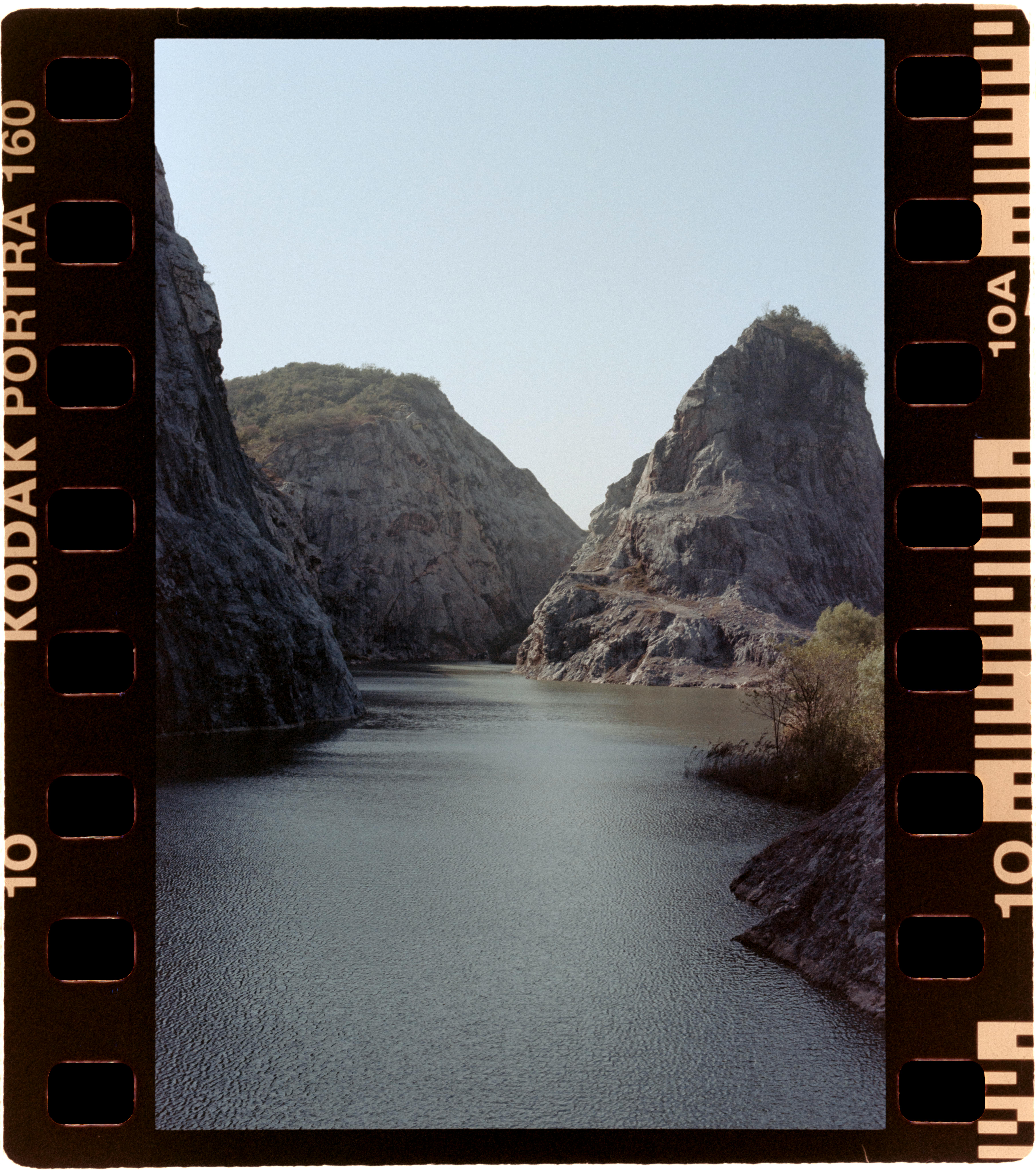 A stunning view of a tranquil river flowing between rugged rocky cliffs under a clear sky.