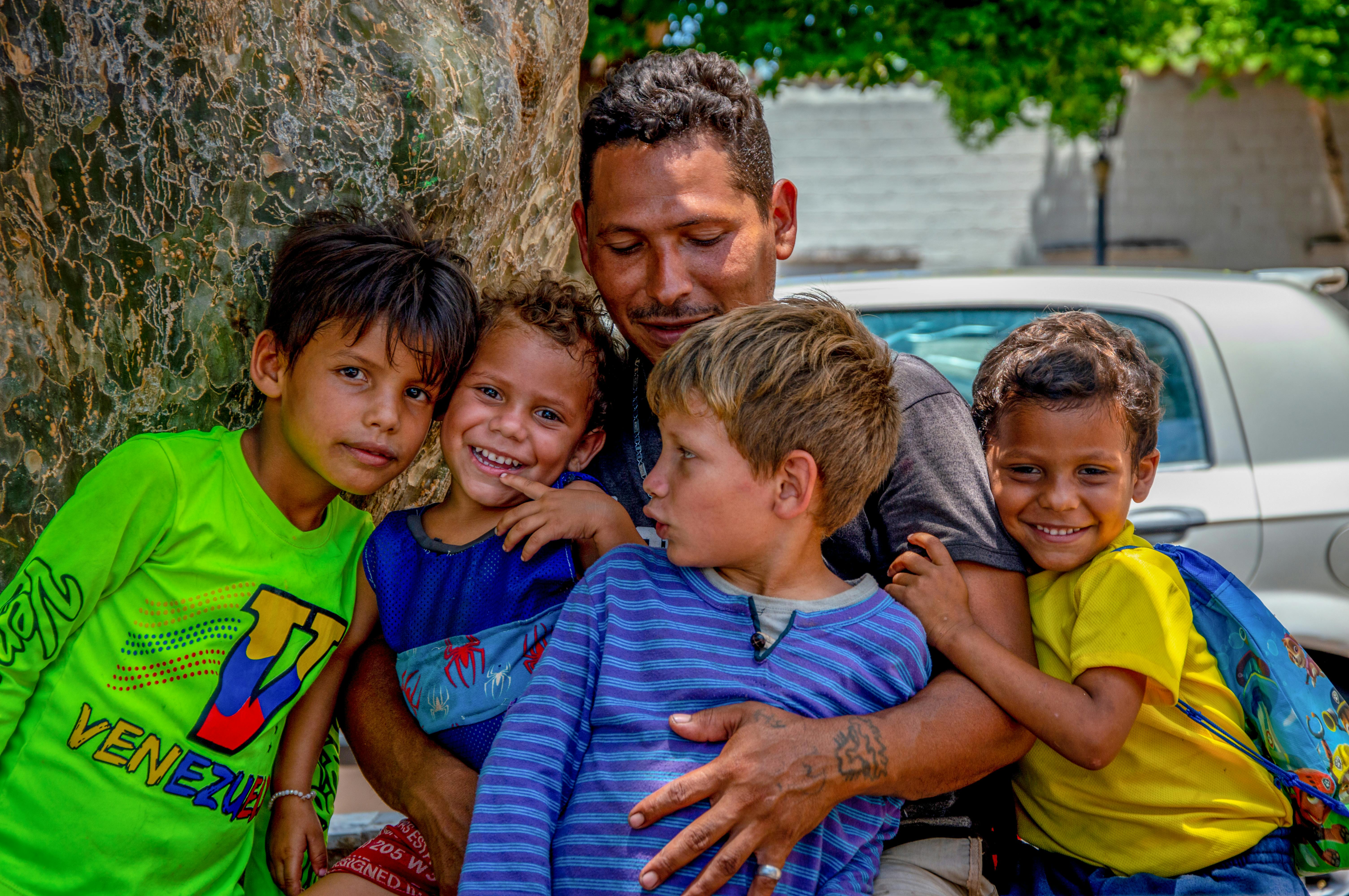 A man stands with his children, all smiling and posing together for a family photograph.