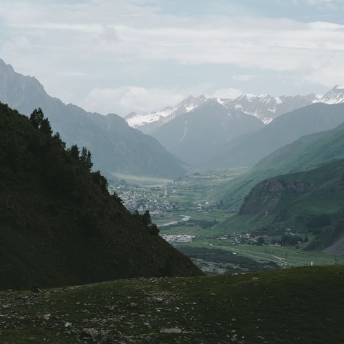 Free Breathtaking view of a lush green valley surrounded by towering mountains with snowy peaks. Stock Photo