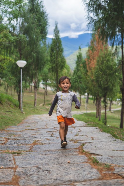 Free A happy child walking on a stone path surrounded by lush greenery in the mountains of Paro, Bhutan. Stock Photo