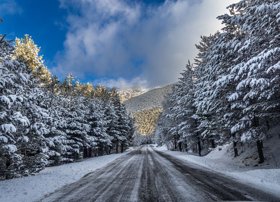A picturesque winter road through snow-covered coniferous forest in Andorra, under a vibrant blue sky.