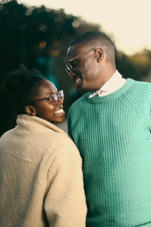 A couple in glasses and green sweaters smiling at each other