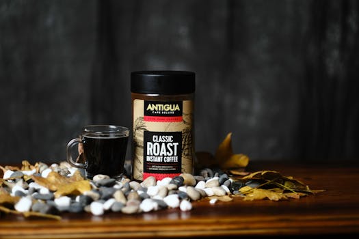 A still life of Antigua Classic Roast Instant Coffee with autumn leaves and pebbles.
