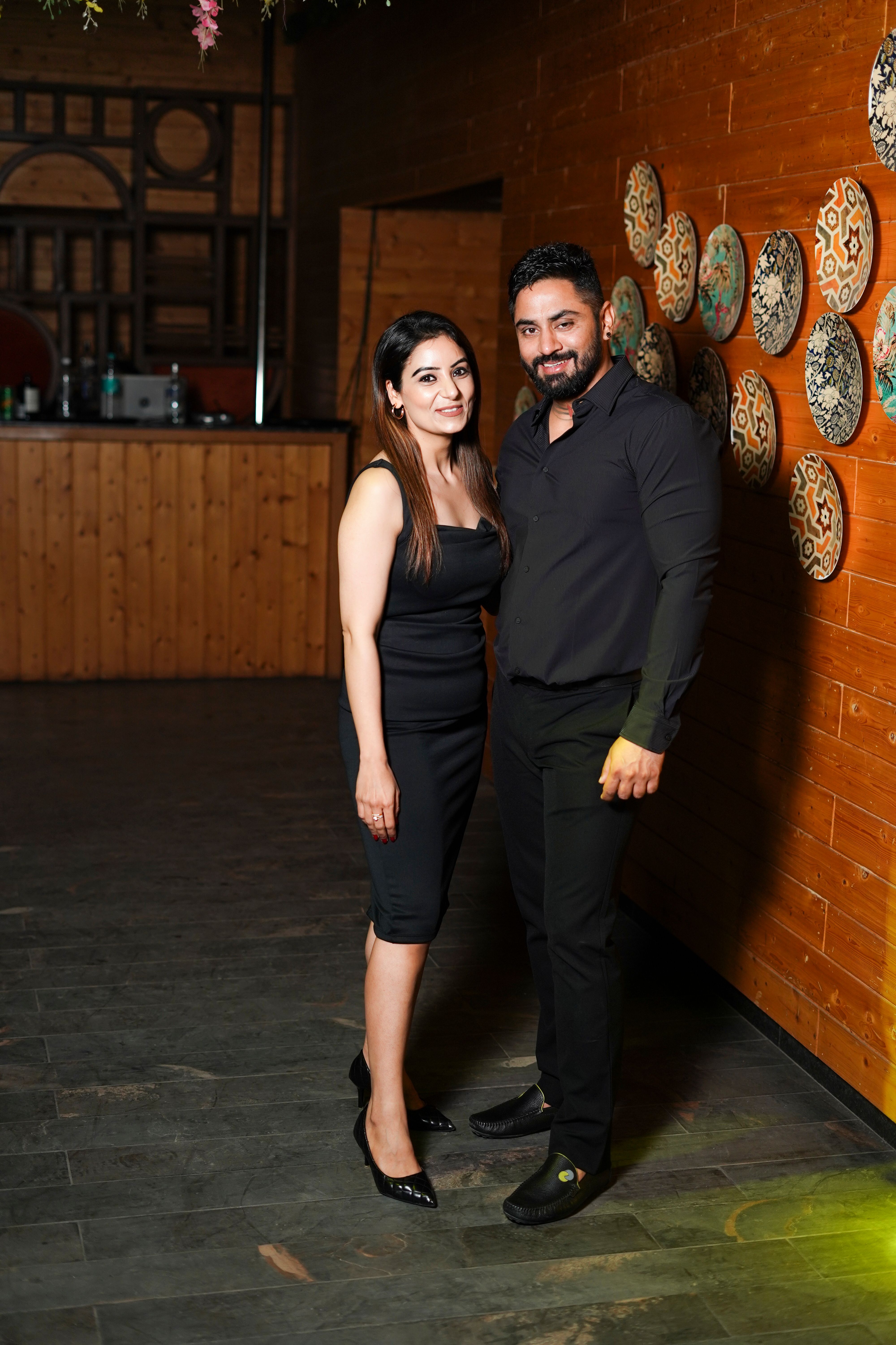 Elegant couple in black attire posing together indoors, exuding style and confidence.