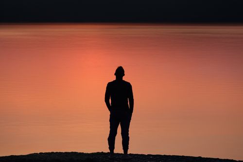 Free A man in silhouette stands by a peaceful lakeshore during sunset in Stamford, CT. Stock Photo