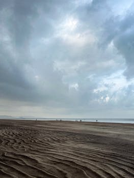 A peaceful beach scene with dramatic clouds and rippled sand under a soft light.