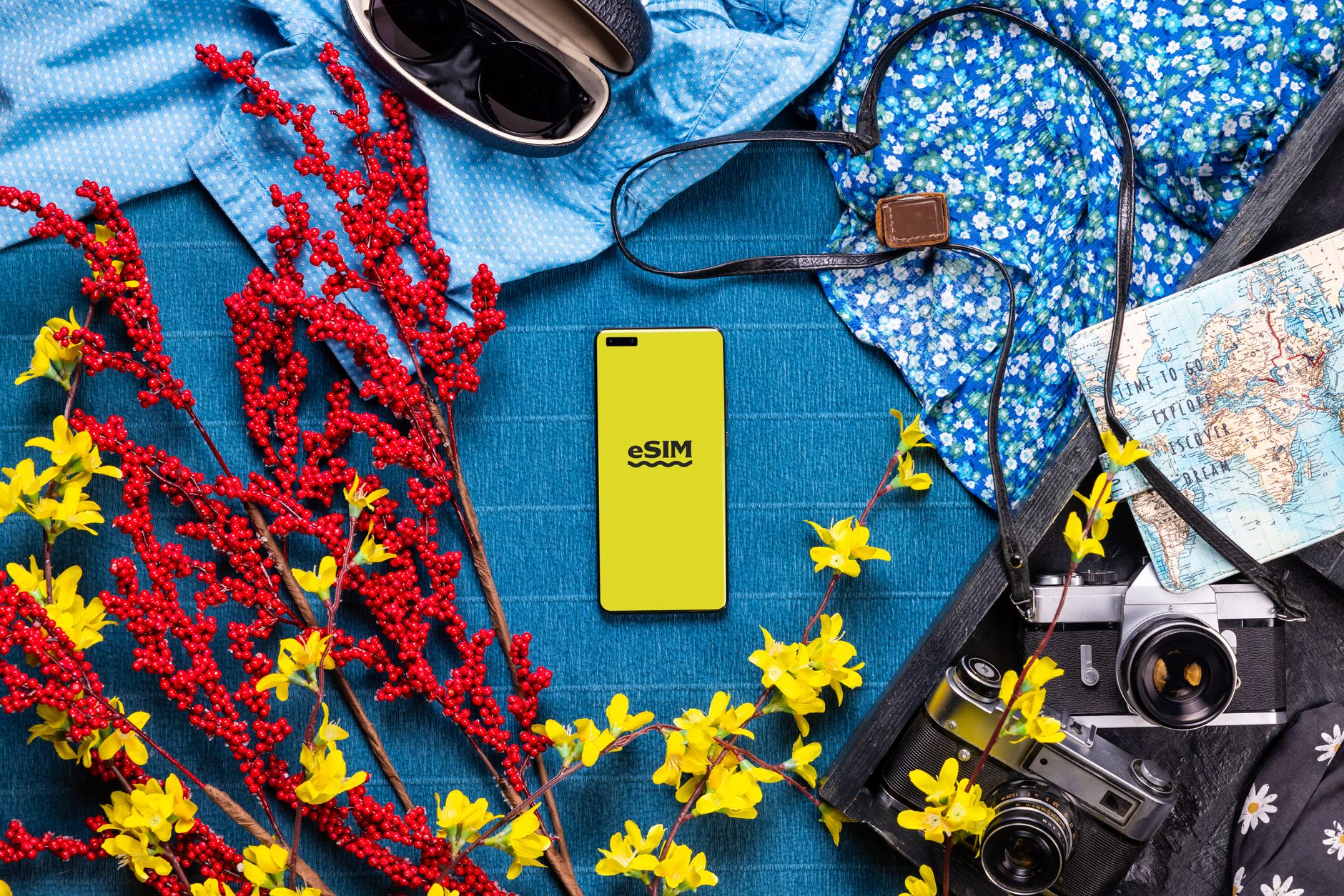 Flat lay of travel essentials including smartphone, camera, and vibrant flowers on a colorful background.