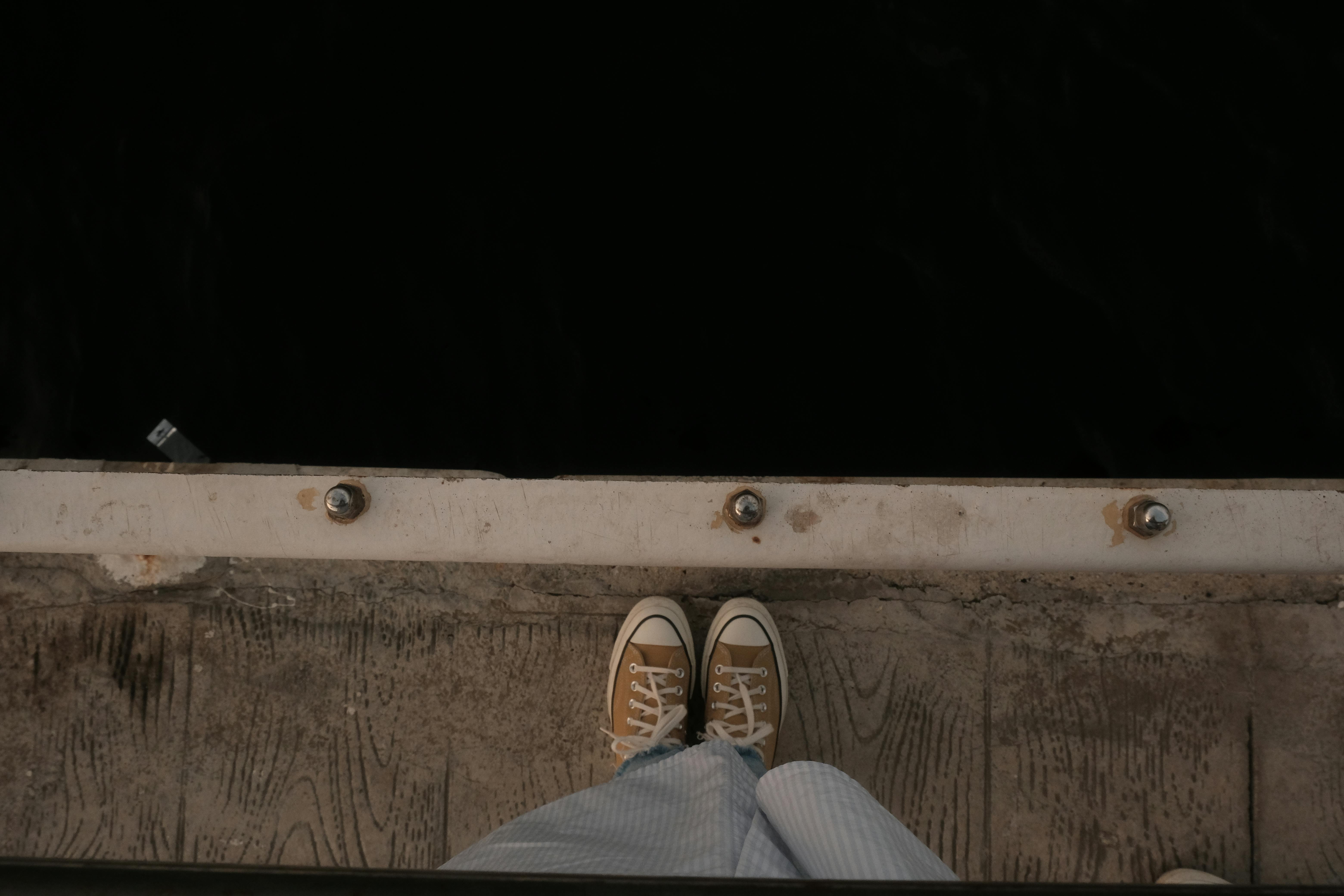 A unique perspective of shoes standing on a weathered pier, overlooking calm dark water.