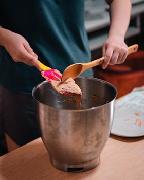 Person mixing dough in a metal bowl with a colorful spatula in the kitchen.