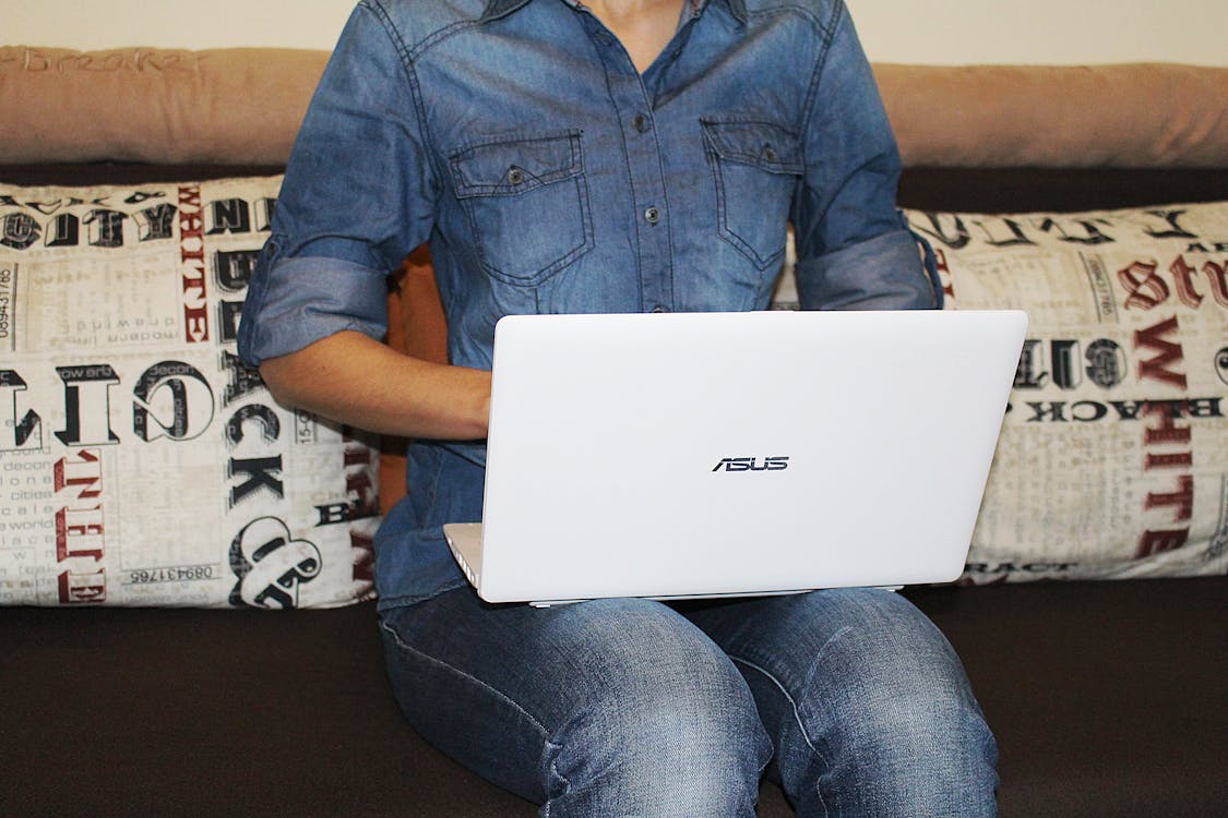 Person in Blue Dress Shirt Sitting on Couch While Using White Asus Laptop