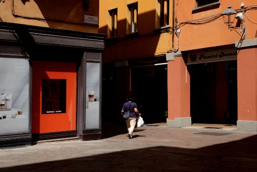 A lone pedestrian walks down a shadowy street in a European city.