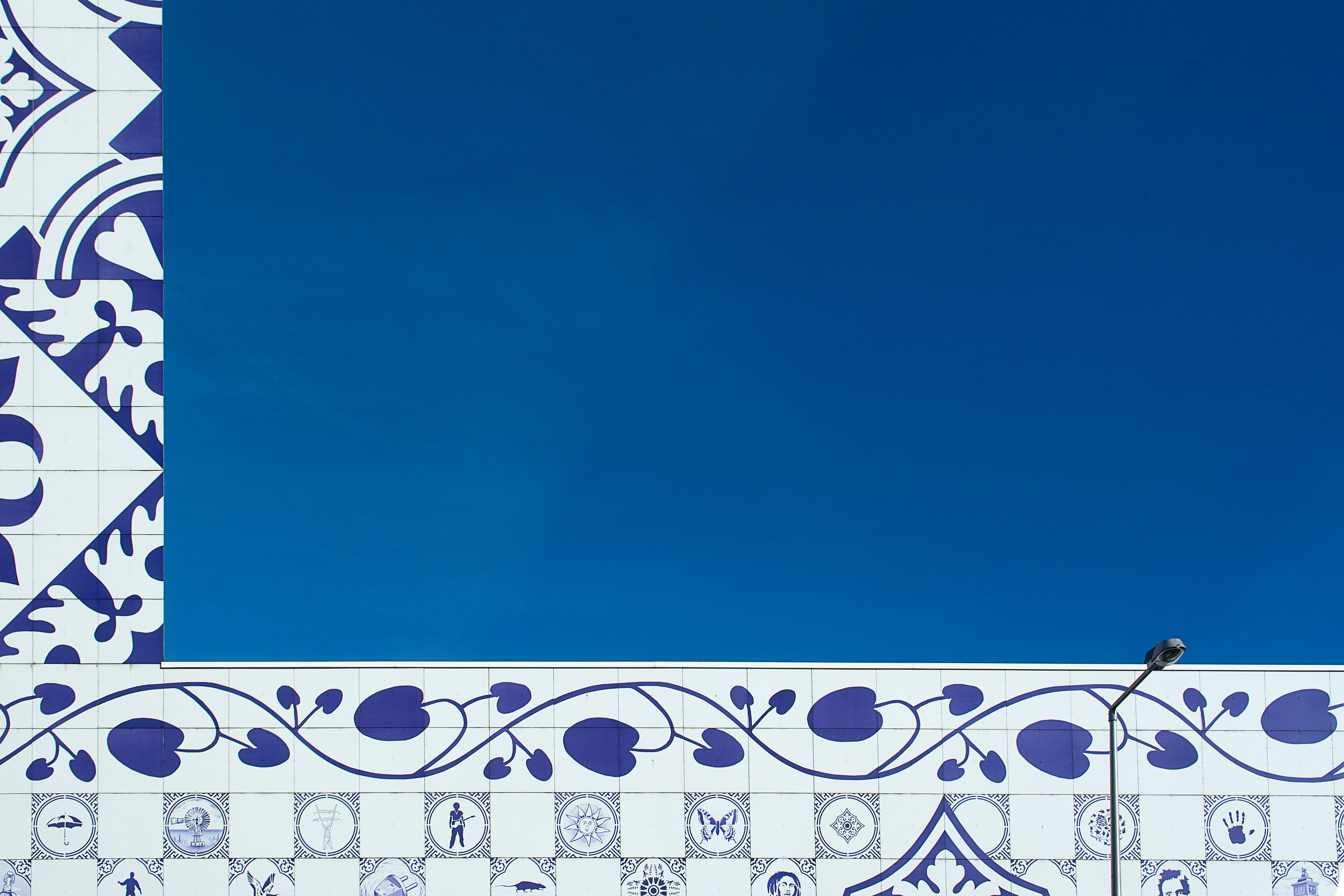 Artistic blue and white ceramic tile wall against a clear sky, with decorative floral patterns.